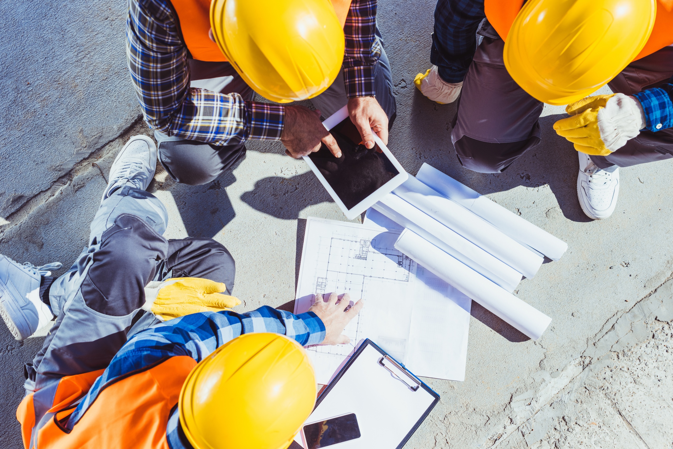 Three construction workers sitting on concrete and discussing building plans